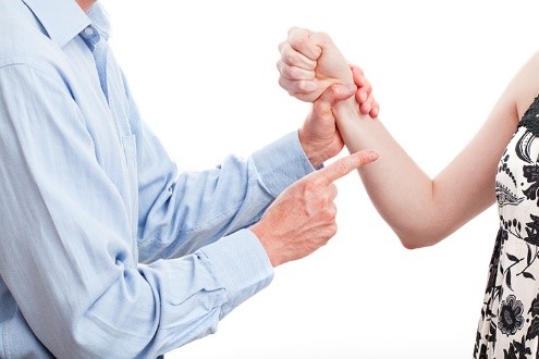 A man grabbing a woman by the wrist and pointing at her with his other hand. The woman is trying to get away.