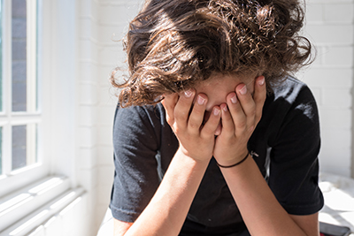 A teenage boy sitting on the ground with his arms on his legs, looking sad